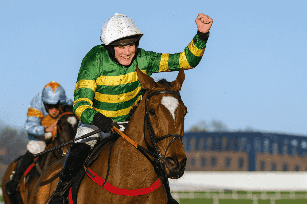 Jockey wearing green and yellow silks celebrates victory on a Henry de Bromhead-trained horse during a National Hunt race, raising his arm in triumph as the horse crosses the finish line.