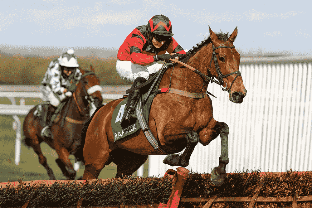 A National Hunt race featuring a leading horse ridden by a jockey in Lucinda Russell’s red and black silks, clearing a hurdle ahead of a rival during the 2025/2026 jumps season.